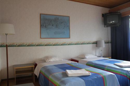 a hotel room with two beds and a tv at Hotel Tulikettu in Sotkamo