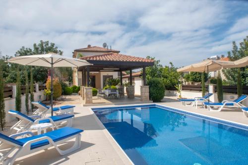 a pool with chairs and umbrellas next to a house at Kallizoni villa in Paphos City