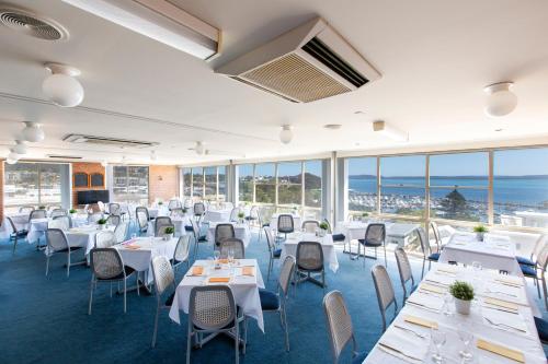 a restaurant with white tables and chairs and windows at Marina Resort in Nelson Bay