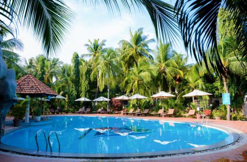 una piscina in un resort con palme e ombrelloni di Four Oceans Beach Resort - Bon Bien Mui Ne a Mui Ne