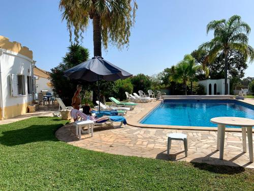 a pool with people sitting on chairs and an umbrella at Quinta Shiamar in Quarteira
