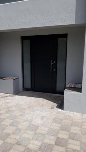 eine schwarze Tür eines Gebäudes mit zwei Fenstern in der Unterkunft Shell Cottage a stone's throw from the beach in Langebaan