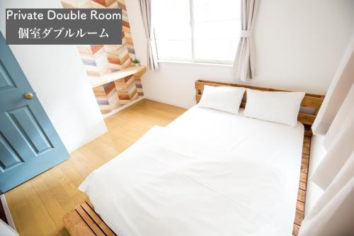a bedroom with a bed with white sheets and a window at IZA Enoshima Guest House and Bar in Fujisawa