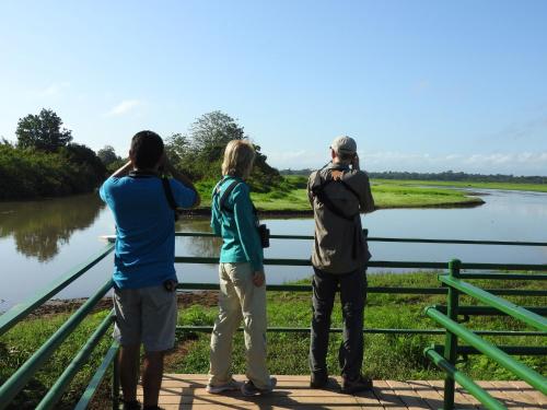 drie mensen op een brug die naar een rivier kijken bij Hotel de Campo Caño Negro in Caño Negro