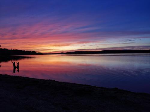 two people walking on the shore of a lake at sunset at By The River B&B in Fredericton
