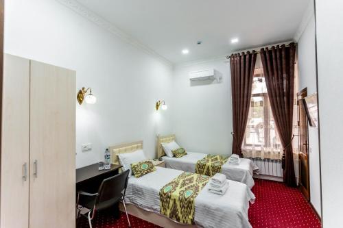 a room with two beds and a desk and a window at Hotel Suzani Samarkand in Samarkand