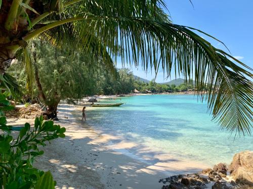 a person standing on a beach with a boat in the water at Coconut Beach Bungalows in Chaloklum