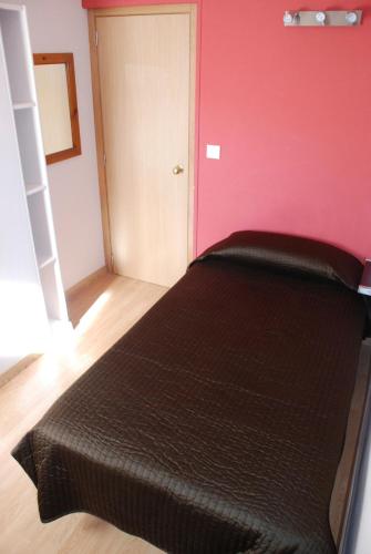 a black bed in a room with a pink wall at Hostal Delgado in Benabarre