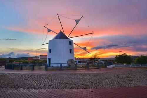 a white windmill with a sunset in the background at Casa da Aldeia - Guest House in Odiáxere