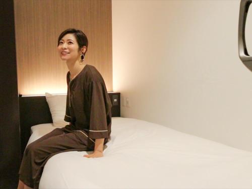 uma mulher sentada em cima de uma cama em LEO YU Capsule Hotel Nishifunabashi em Funabashi