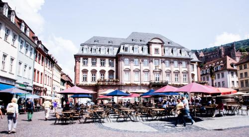 un groupe de tables et de chaises avec parasols devant un bâtiment dans l'établissement Hotel am Rathaus, à Heidelberg