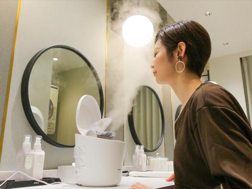 a woman standing in front of a bathroom mirror at Leo Yu Capsule Hotel Funabashi in Funabashi