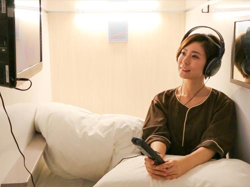 une femme portant des écouteurs et tenant une télécommande dans l'établissement Leo Yu Capsule Hotel Funabashi, à Funabashi