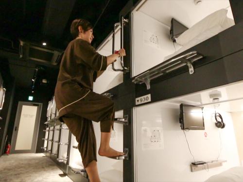 船橋的住宿－Leo Yu Capsule Hotel Funabashi，一位在客房内双层床上行走的人