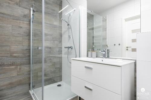 a white bathroom with a shower and a sink at Jantar Apartamenty - Holiday Polanki Park SPA in Kołobrzeg