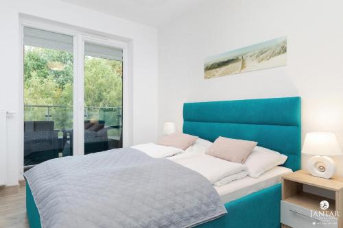 a bedroom with a blue and white bed and a window at Jantar Apartamenty - Holiday Polanki Park SPA in Kołobrzeg