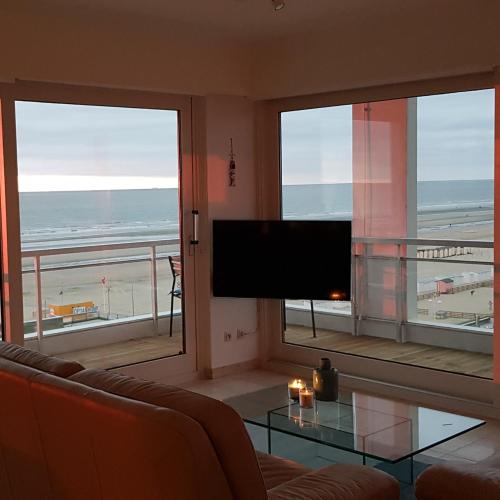 een woonkamer met een televisie en uitzicht op het strand bij 7th Heaven Seaview in De Panne