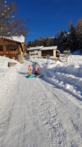 two children are skiing down a snow covered road at Guardamunt in Scuol