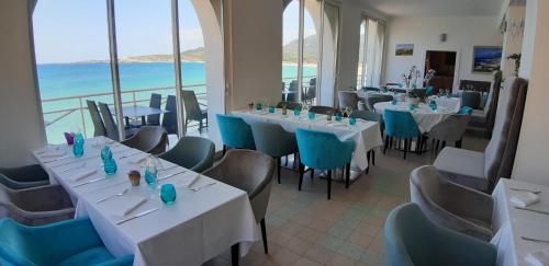a restaurant with white tables and chairs and the ocean at Hotel de la Plage Santa Vittoria in Algajola