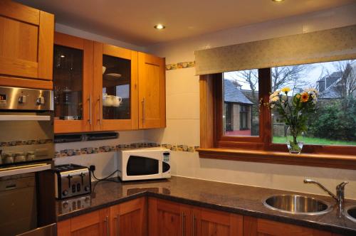 a kitchen with wooden cabinets and a microwave and a window at Inveroran in Campbeltown