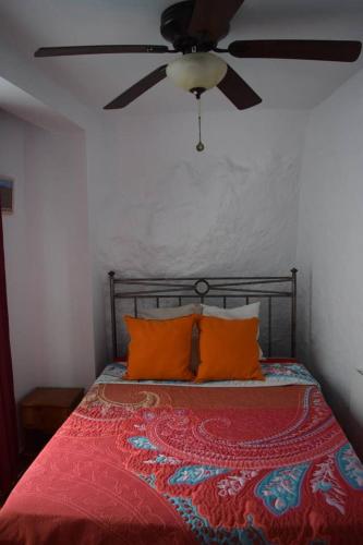 a bed with orange pillows and a ceiling fan at Casa Amado in Olvera