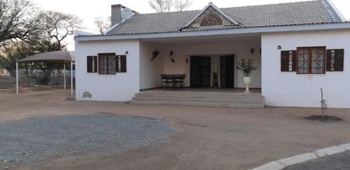 Biały dom z brązowymi oknami i werandą w obiekcie Nooitgedacht Self Catering CC w mieście Okahandja