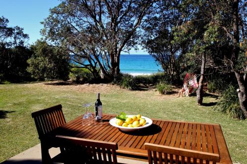 a wooden table with a bowl of fruit and a bottle of wine at Absolute Beachfront Mollymook in Mollymook