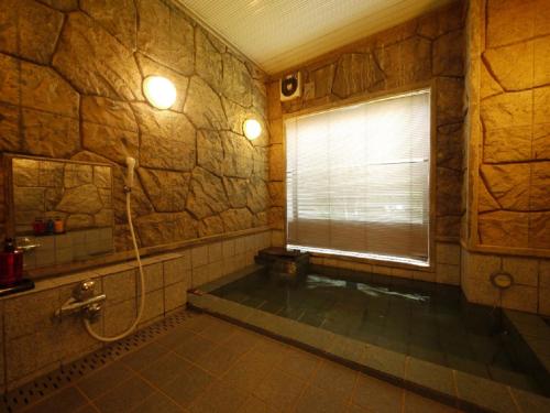 La salle de bains en pierre est pourvue d'une baignoire et d'une fenêtre. dans l'établissement Hotel Route-Inn Court Minami Matsumoto, à Matsumoto