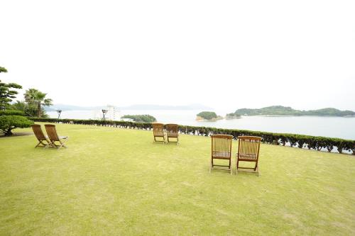 a row of chairs sitting on the grass near the water at Tenku Hotel Kairo in Tonosho