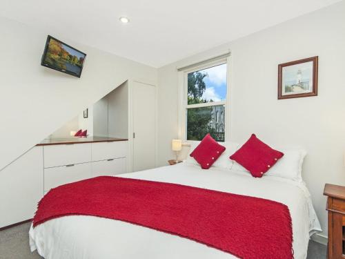 biała sypialnia z dużym łóżkiem z czerwonymi poduszkami w obiekcie Johanssons Perch Cottage w mieście Port Fairy