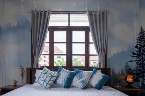 a bed with blue and white pillows in front of a window at Baan Suan Krung Kao in Phra Nakhon Si Ayutthaya