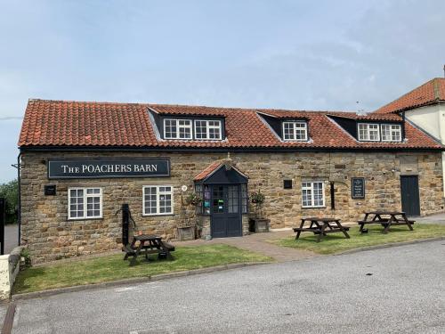a building with two picnic tables in front of it at Poacher's Barn in Cayton