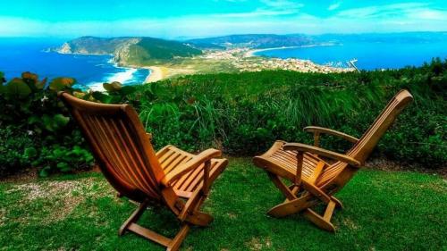 dos sillas de madera sentadas en la hierba cerca del océano en Apartamentos SEOANE, en Finisterre