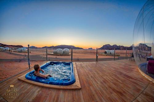 a young boy sitting in a hot tub on a deck at Wadi Rum Bubble Luxotel in Wadi Rum