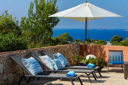 a patio with two benches and an umbrella at CAN COSTA Amazing view of sunset on the sea in Cala Vadella
