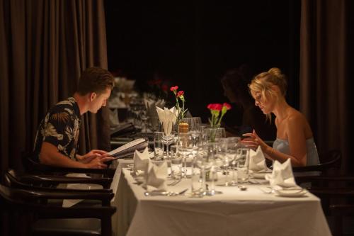 a man and woman sitting at a table looking at their cell phones at Scarlet Pearl Cruises - Wonder On Lan Ha Bay in Ha Long