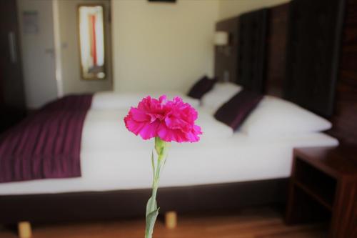 a pink flower in a vase in front of a bed at Hotel Germersheimer Hof in Germersheim