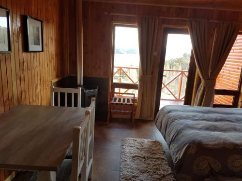 1 dormitorio con cama, mesa y balcón en Patagonia Acres Lodge, en Mallin Grande