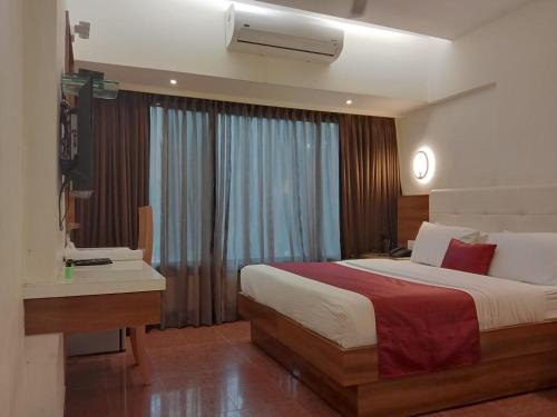 a bedroom with a bed and a desk and a window at Hotel Milan International in Mumbai