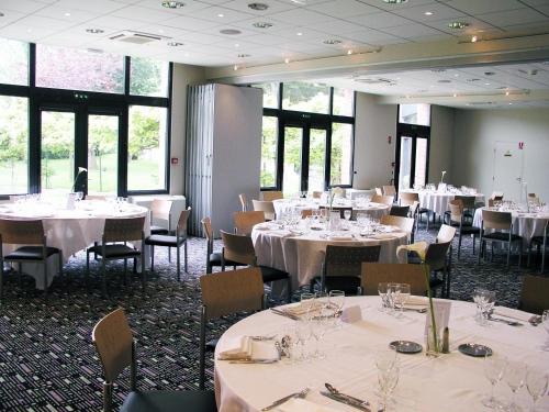 a dining room with white tables and chairs and windows at Hotel du Casino in Saint-Valéry-en-Caux