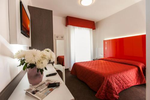 ein Schlafzimmer mit einem Bett und einer Vase aus Blumen auf einem Tisch in der Unterkunft Hotel Lilia in Lido di Jesolo