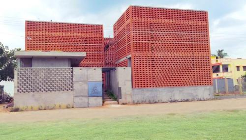 two tall red brick buildings with a field in front at Sengal Boutique Hotel in Auroville
