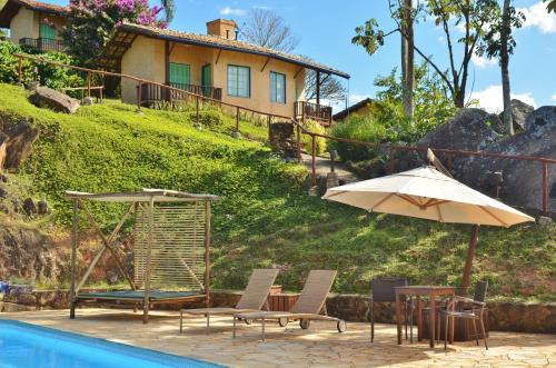 a pool with chairs and an umbrella and a house at Cafezal em Flor Turismo e Cafés Especiais in Monte Alegre do Sul