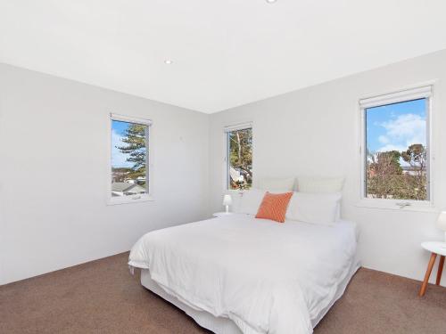 a white bedroom with a bed and two windows at Riverend Regent in Port Fairy