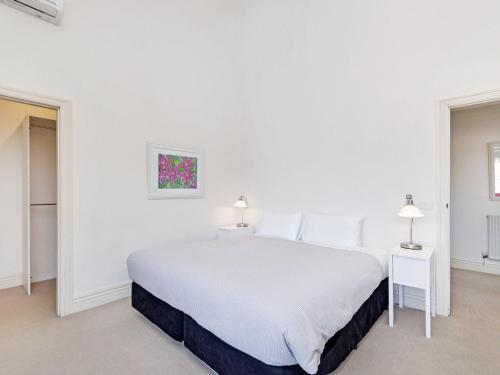 a white bedroom with a white bed and two lamps at Shearwater Penthouse in Port Fairy