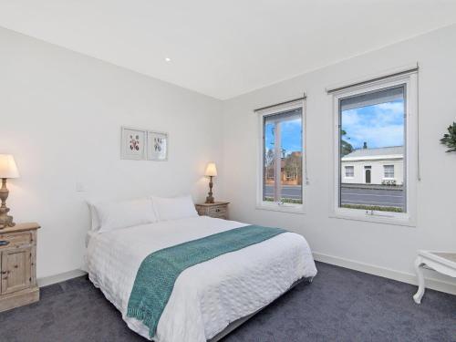 a white bedroom with a bed and two windows at The Craic in Port Fairy