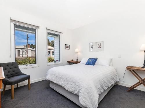a white bedroom with a bed and a chair at The Townhouse in Port Fairy