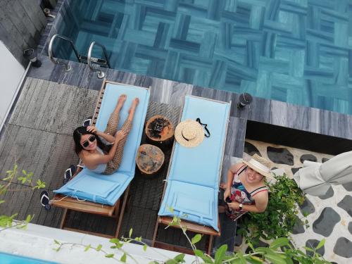 twee personen in stoelen naast een zwembad bij Santori Hotel Da Nang Bay in Da Nang