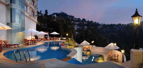 einen Pool mit Tischen und Stühlen neben einem Gebäude in der Unterkunft Radisson Hotel Shimla in Shimla
