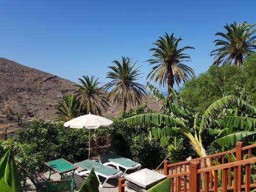 un patio con sillas, sombrilla y palmeras en Finca Ossorio Casa Rita, en Vallehermoso